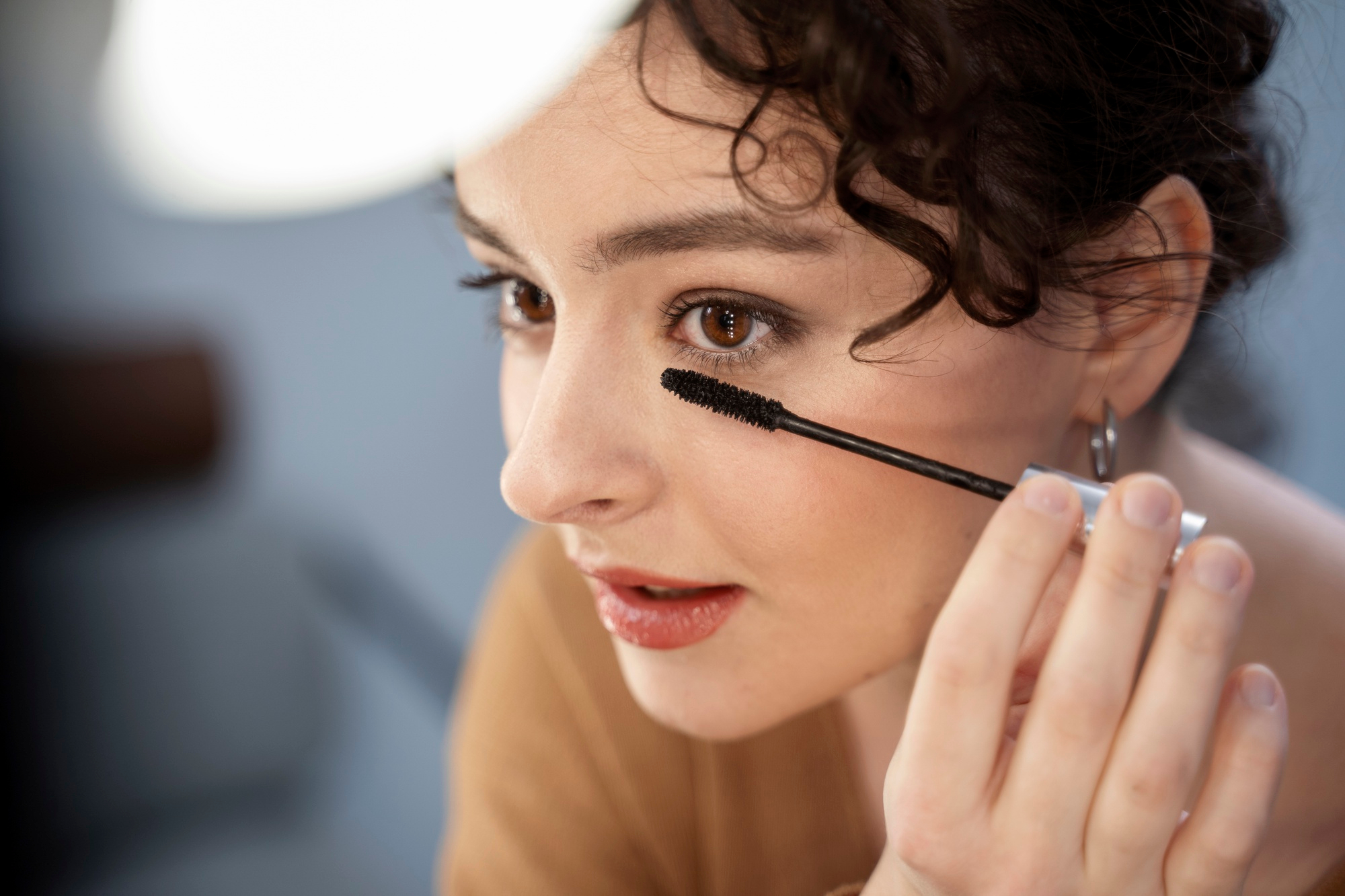 Close-up of a hand gently applying eyelash serum along the lash line. The serum is applied with a thin brush to enhance lash growth.